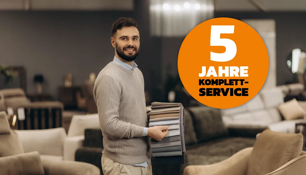 Freundlicher Verkäufer im Möbelhaus zeigt verschiedene Stoffmuster für Sofas und Polstermöbel, Beratung für individuelle Stoffwahl und hochwertige Polsterbezüge.